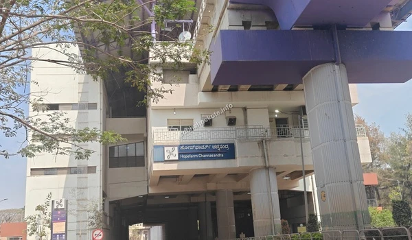 A daytime view of the Hopefarm Channasandra metro station building, highlighting the signage and the elevated purple line infrastructure in Whitefield.