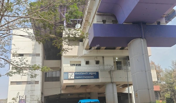 An eye-level shot of a Namma Metro station entrance in Whitefield, displaying the industrial design of the transit hub with a blue bus partially visible at the bottom of the frame.