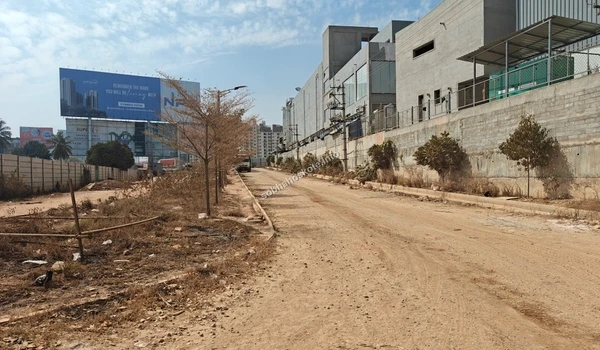 View of the wide entrance access road at Sobha Hoskote showing the construction progress, perimeter fencing, and surrounding infrastructure