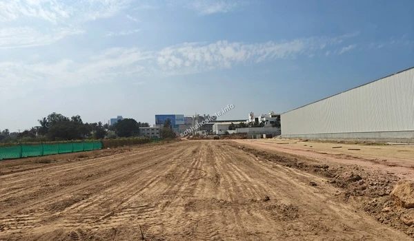 View of the leveled terrain adjacent to existing structures and perimeter fencing at the Sobha Hoskote site