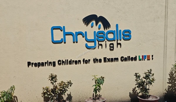 Exterior view of the Chrysalis High entrance wall near Sobha Hoskote surrounded by greenery and featuring the school's distinctive blue and black logo