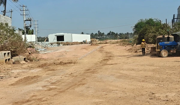 Grand entrance view of Sobha Hoskote from the main highway showing the access road, site hoarding, and surrounding industrial infrastructure