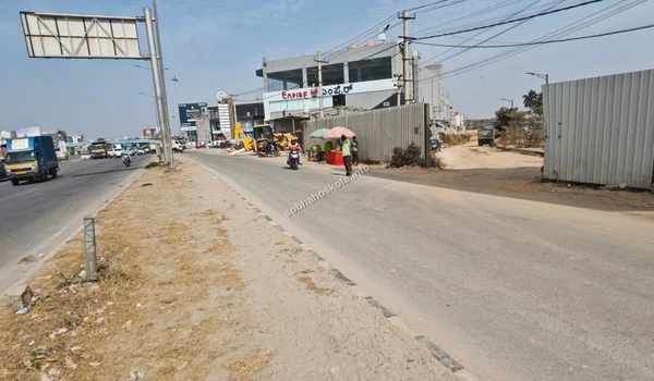 A perspective view from the highway showing the surrounding commercial buildings and the dedicated access lane leading toward Sobha Hoskote