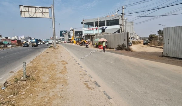A long dirt access road within the Sobha Hoskote development area showing the perimeter wall and proximity to local landmarks