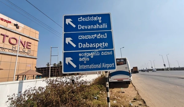 A perspective view of the modern road infrastructure along the STRR highway towards Devanahalli, featuring safety barriers and palm-lined surroundings