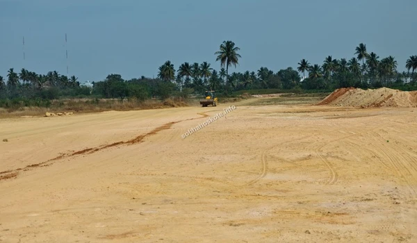 View of the site perimeter showing the leveled ground adjacent to the large warehouse facilities at Sobha Hoskote
