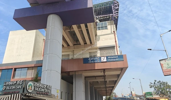 Exterior of Whitefield Kadugodi Metro Station showing the purple line pillar, station signage, and the nearby Silicon Cafe.